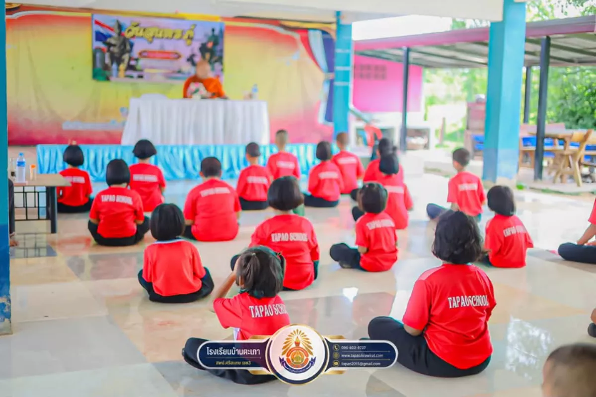 นักเรียนโรงเรียนบ้านตะเภาในเสื้อกีฬาสีแดงนั่งฟังการอบรมจากพระธรรมทูตที่อาคารอเนกประสงค์